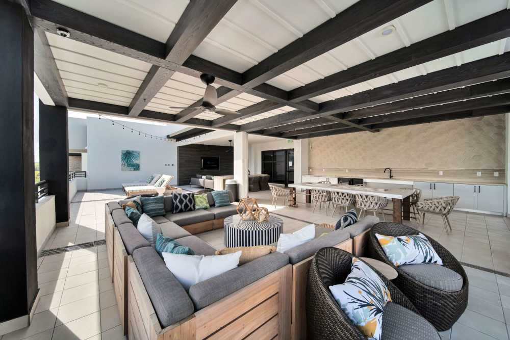 Two-Bedroom Luxury Apartments In Doral, FL - Palmera - Elevated Sun Lounge With A Kitchen Area, Dining Table And Chairs, Couch Seating, Strung Outdoor Lights, And Lounge Chairs